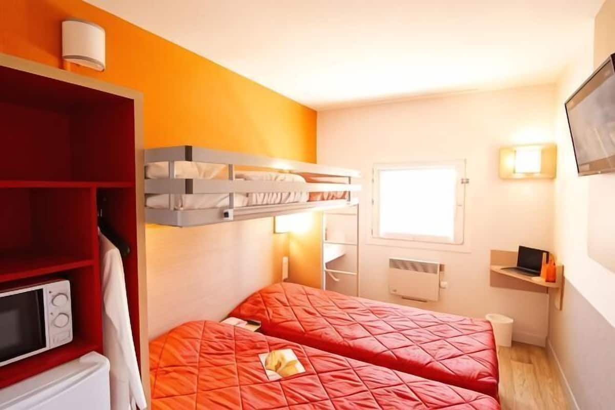 A compact room with a bunk bed, a microwave, a small desk with a laptop, and a TV on the wall.