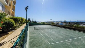 En utomhus tennisbana med nät, omgiven av ett grönt staket och en gångstig.