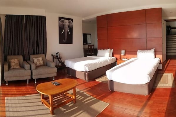 Una habitación de hotel con dos camas, un sofá, una mesita de centro de madera y un cuadro grande de un elefante en la pared.