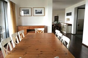 Un comedor con una mesa de madera y sillas blancas, un armario de madera y cuadros en la pared.