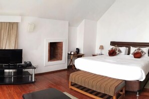 Una habitación de hotel con una cama grande, televisor, una mesita con lámpara y una chimenea.