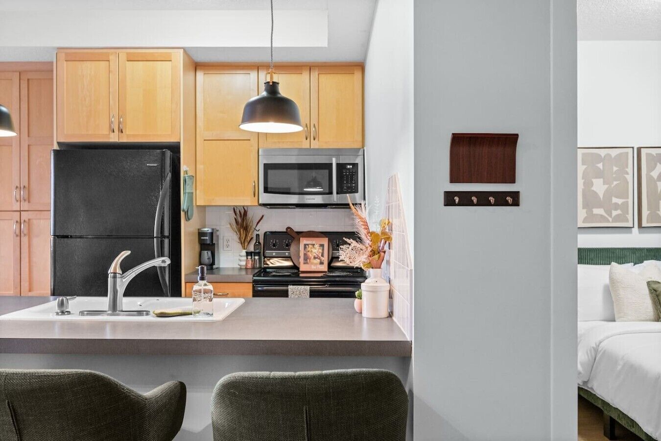 A modern kitchen with wooden cabinets, a black refrigerator, a microwave, and a gas stove. There is a small dining area with two chairs.