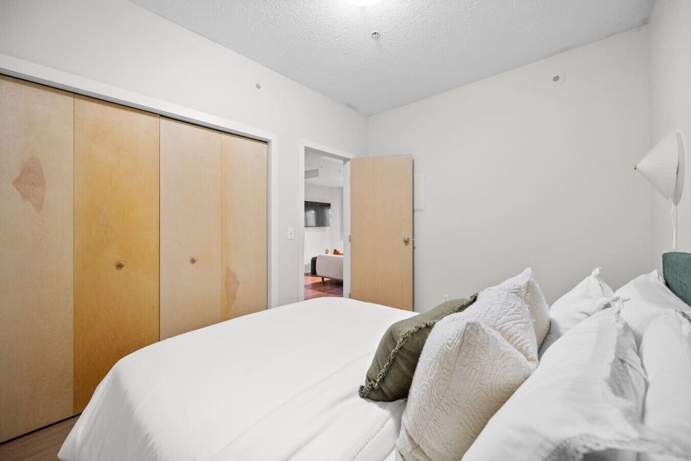 Une chambre à coucher avec un lit, du linge de lit blanc, un oreiller vert, une armoire en bois et un plafond blanc.