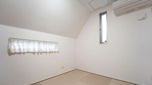 Una habitación con techo inclinado, ventana y cortina en la pared.