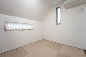 A room with a sloped ceiling, a window, and a curtain on the wall.