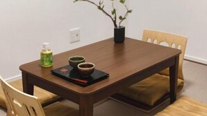 Una mesa de madera con dos cuencos y una botella, una planta en maceta y una silla con cojín.