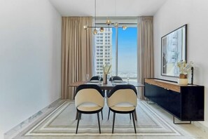 A modern dining area with a table, chairs, a black console, and a large window with a city view.