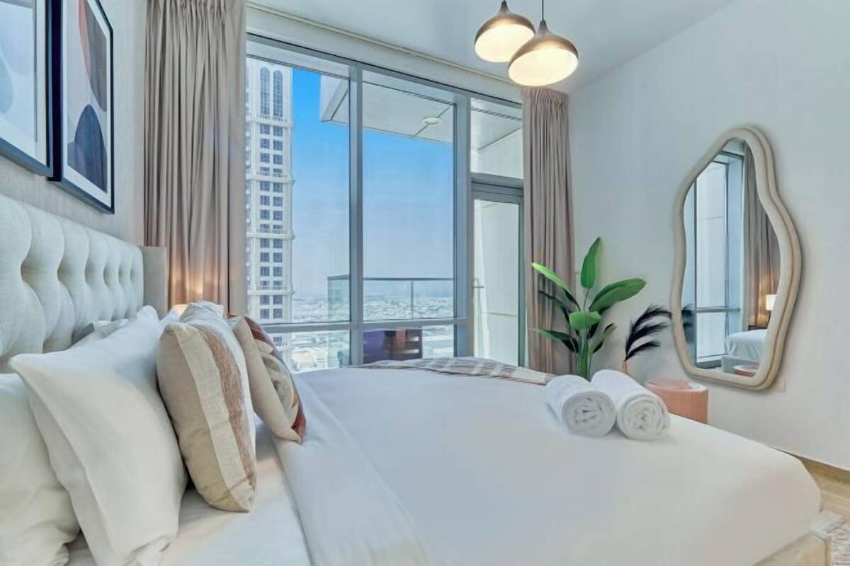 Habitación de hotel moderna con una cama grande, vistas a la ciudad, un espejo y una planta.