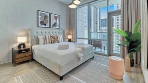 A modern hotel room with a large bed, a nightstand, a lamp, a large window with a view of buildings, and a potted plant. - bnbme Classic 1BR 8 mins to Burj Khalifa (Dubai)