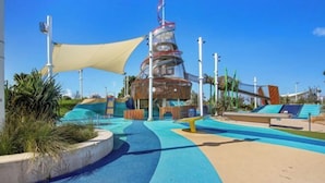 A children's play area with a climbing structure, shaded seating, and a pool. - Skyline Showdown - Views, Games & Vibes (Southport)