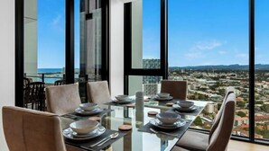 A dining area with a glass table and chairs, overlooking a cityscape. - Skyline Showdown - Views, Games & Vibes (Southport)