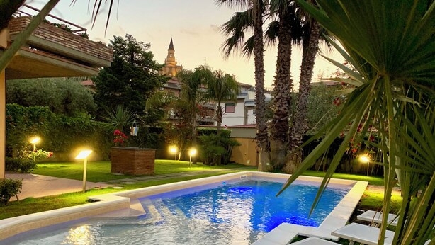 An outdoor swimming pool with lounge chairs, surrounded by palm trees and a well-lit garden area. - Etna Villa Alba Chiara (Trecastagni)