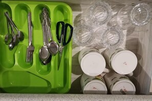 Et tekøkken med en grøn utensilholder, forskellige køkkenredskaber og flere klare glas og krus.