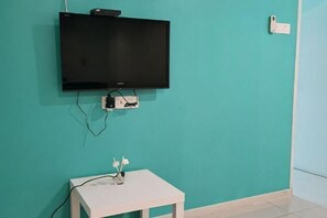 A teal wall with a mounted television, a white table with a vase, and a power outlet. - Peaceful 1-Bedroom Unit at Marina Island by JoMy Homestay (Manjung)