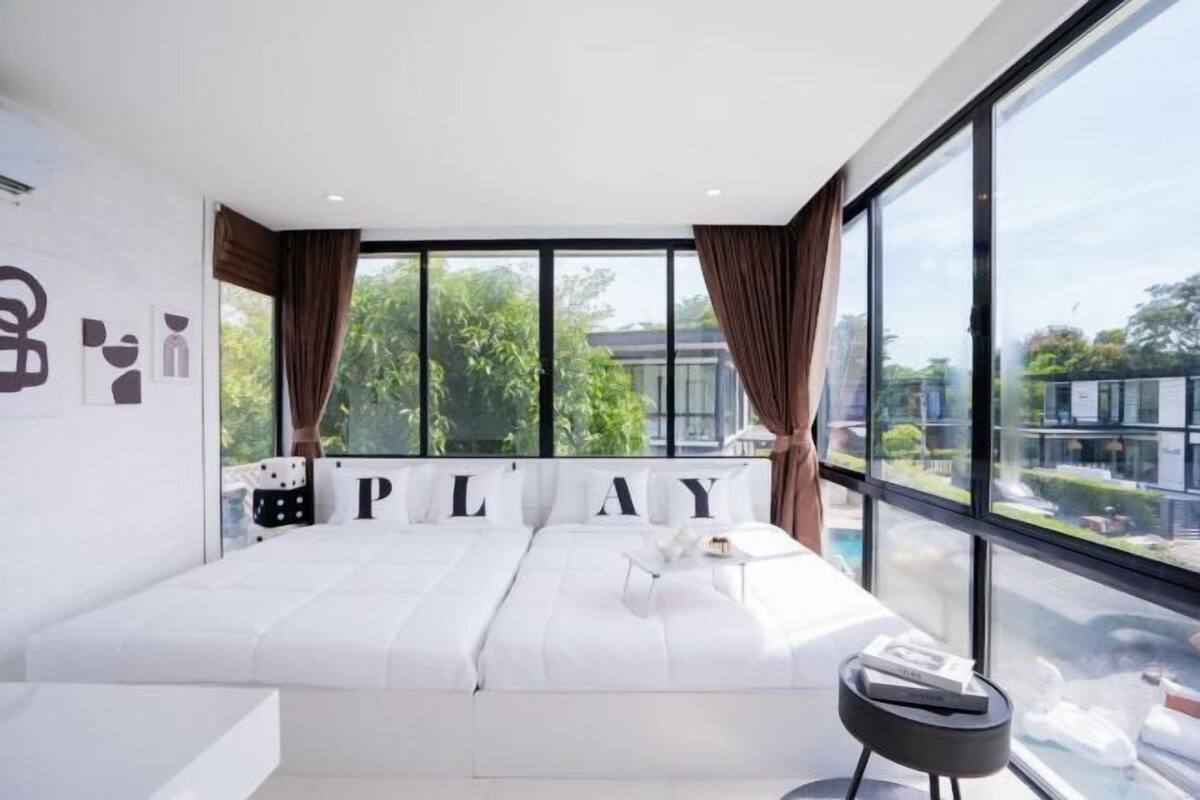 A modern bedroom with a large bed, a view of greenery outside, and a window with curtains.