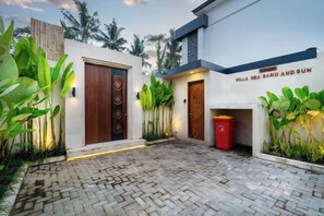 Une villa moderne dotée d’une cour dallée, de grandes fenêtres et d’une enseigne indiquant « Villa Sable, Mer et Soleil ».