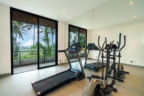A modern gym with a treadmill, elliptical, and stationary bikes, large windows with a view of palm trees. - Villa Sea Sand and Sun by BaliSuperHost (Bali)