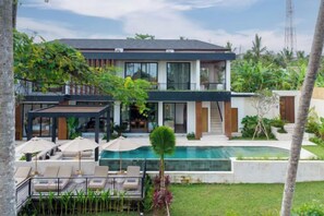 Une maison moderne à deux étages, dotée d’une piscine, d’un espace de détente extérieur et d’une végétation luxuriante.