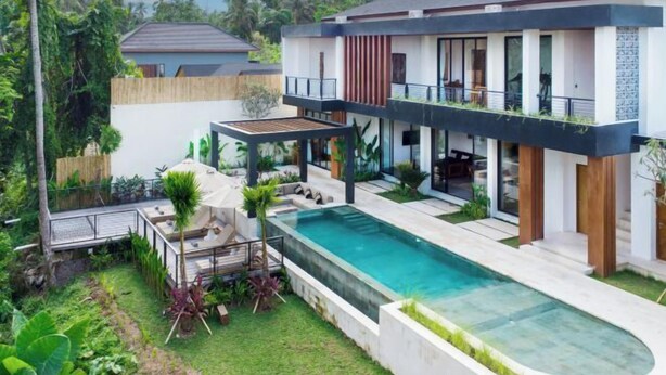 Una casa moderna de dos pisos con piscina, mobiliario exterior y abundante vegetación.