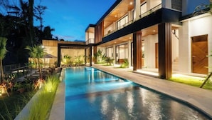 Una casa moderna con piscina, ventanas amplias e iluminación exterior.