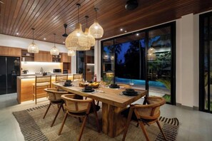 A modern dining area with a wooden table, wicker chairs, and pendant lights. - Villa Sea Sand and Sun by BaliSuperHost (Bali)