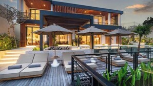 Una casa moderna de dos pisos con piscina, mobiliario exterior y terraza de madera.