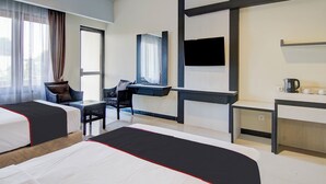 Habitación de hotel con dos camas, un escritorio, una silla, un televisor y una ventana con cortinas.