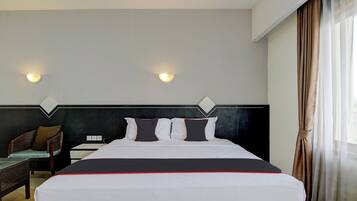 Hotelkamer met een bed, twee wandlampen, een stoel en een raam met gordijnen.