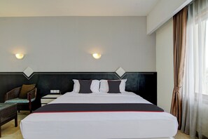 Hotellihuone, jossa on sänky, kaksi seinään kiinnitettyä valaisinta, tuoli ja ikkuna, jossa on verhot.