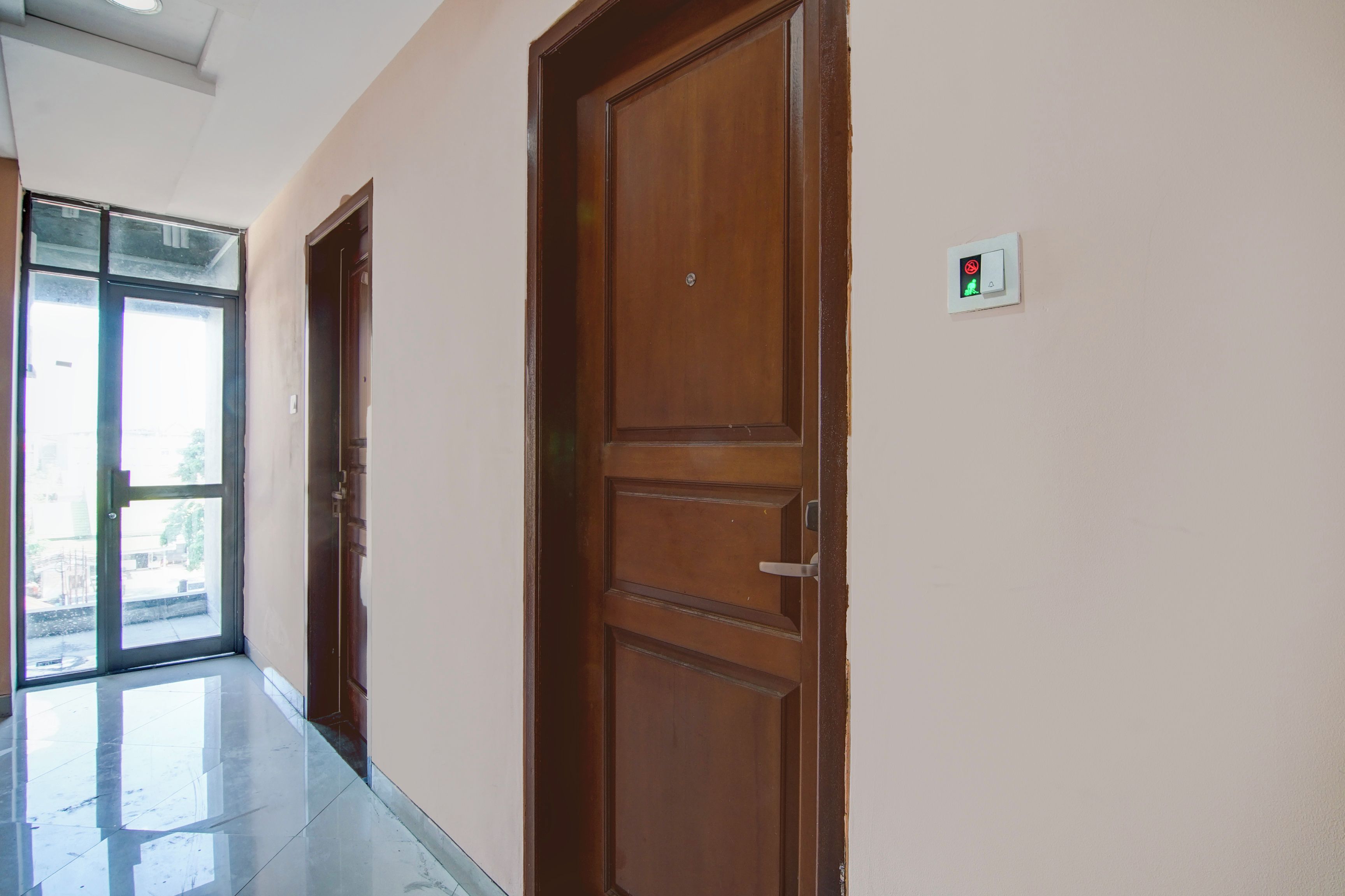 A hallway with wooden doors, a glass door leading outside, and a light switch on the wall.