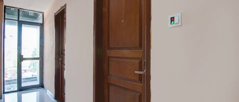 A hallway with wooden doors, a glass door leading outside, and a light switch on the wall.