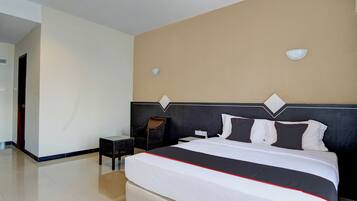 A hotel room with a large bed, a nightstand, a chair, and a wall-mounted light fixture.