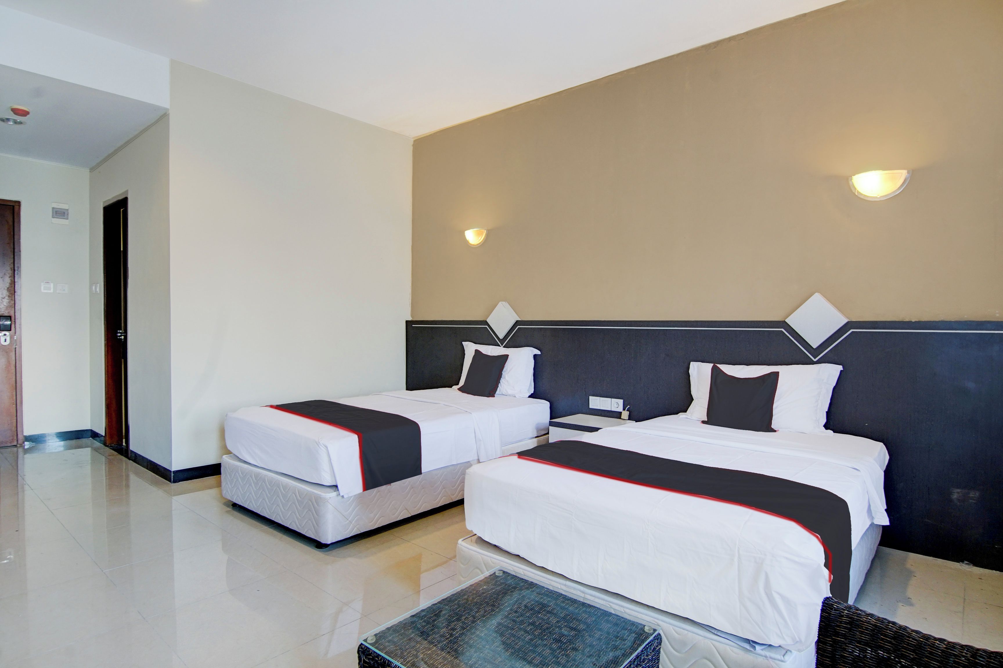 Habitación de hotel con dos camas, una mesita y una lámpara fijada a la pared.