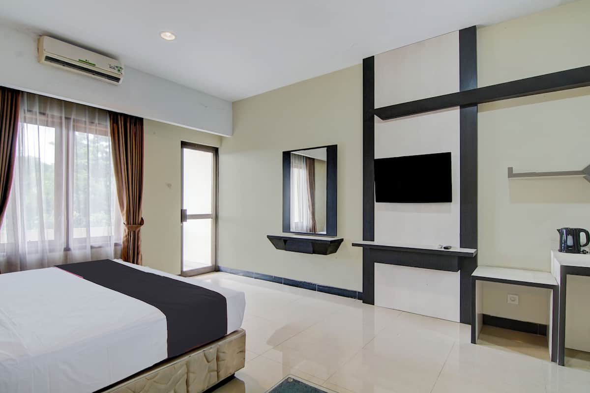 Habitación de hotel con cama, televisor, espejo, una mesita pequeña y aire acondicionado.