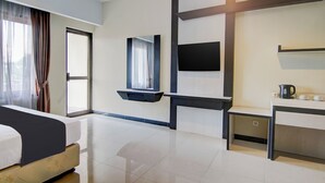 Habitación de hotel con cama, escritorio, televisor de pantalla plana, ventana con cortinas y estante de pared.