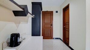 Un pasillo con una puerta de madera, un objeto negro en una estantería y una encimera blanca.