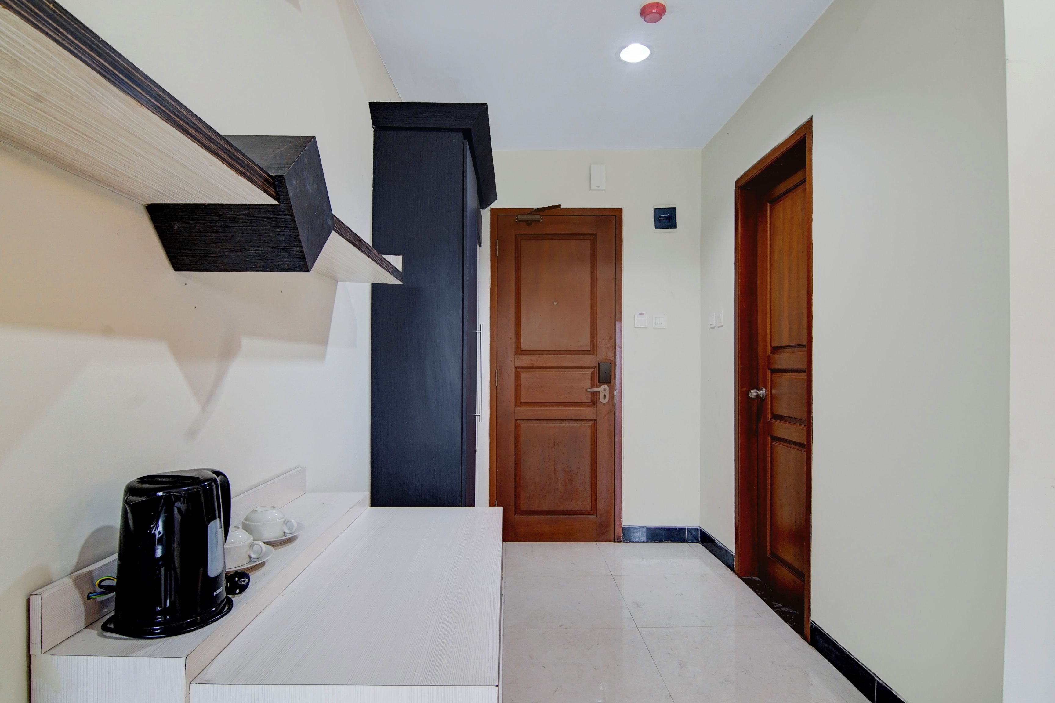 Un pasillo con una puerta de madera, un objeto negro en una estantería y una encimera blanca.