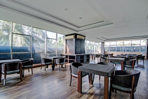 A spacious indoor area with multiple tables and chairs, large windows, and a central air conditioning unit.