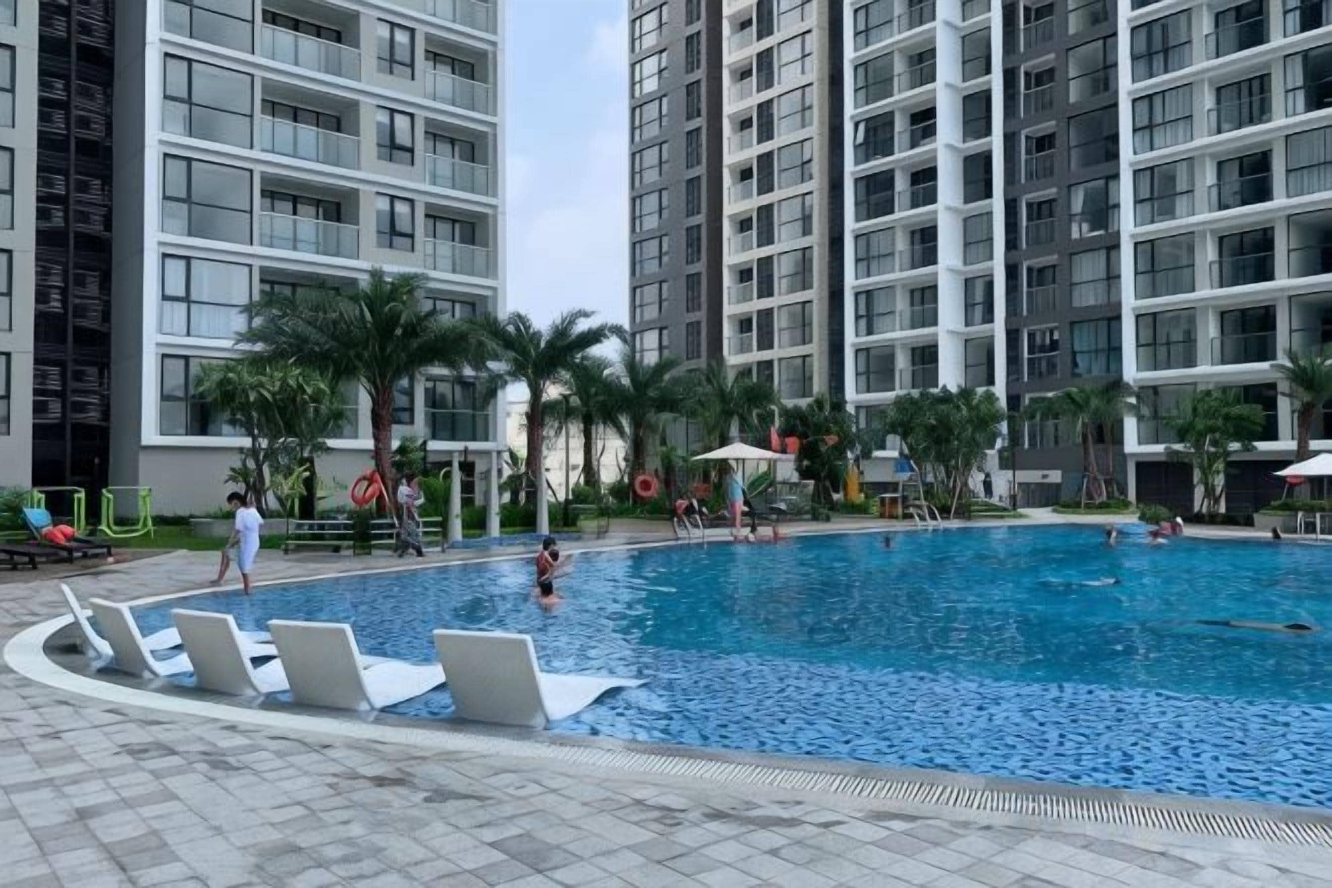 A swimming pool surrounded by high-rise buildings, with lounge chairs and palm trees.