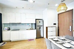 A modern kitchen with white cabinets, a stainless steel refrigerator, and a dining area with a table set for two.