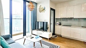 A modern living room with a sofa, coffee table, and a TV. There is a kitchen with white cabinets and a dining area. - Luxury 2Br Vinhomes Skylake - City view/Landmark 72 (Hanoi)