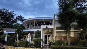 Un edificio moderno con una sección central circular, rodeado por un jardín con arbustos cuidadosamente podados y un sendero pavimentado.