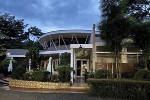 Un edificio moderno con una sección central circular, rodeado por un jardín con arbustos cuidadosamente podados y un sendero pavimentado.