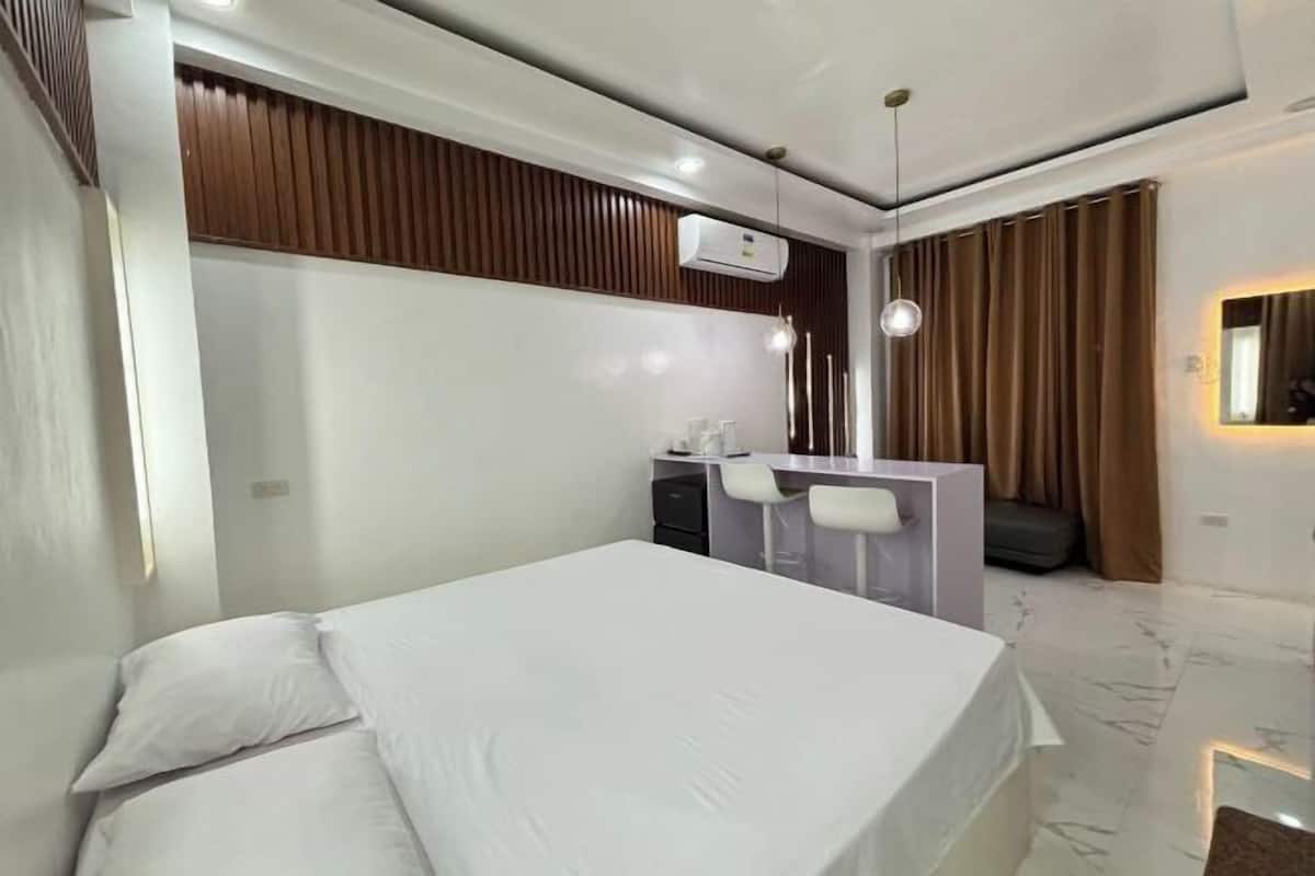 A modern hotel room with a bed, a desk, a chair, a mirror, and a window with curtains.