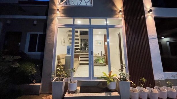 Un edificio moderno con entrada de vidrio, una escalera que conduce al piso superior y plantas en macetas afuera.