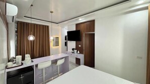 Una habitación de hotel moderna con cama, escritorio con sillas, televisor y minibar.