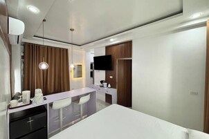 Una habitación de hotel moderna con cama, escritorio con sillas, televisor y minibar.