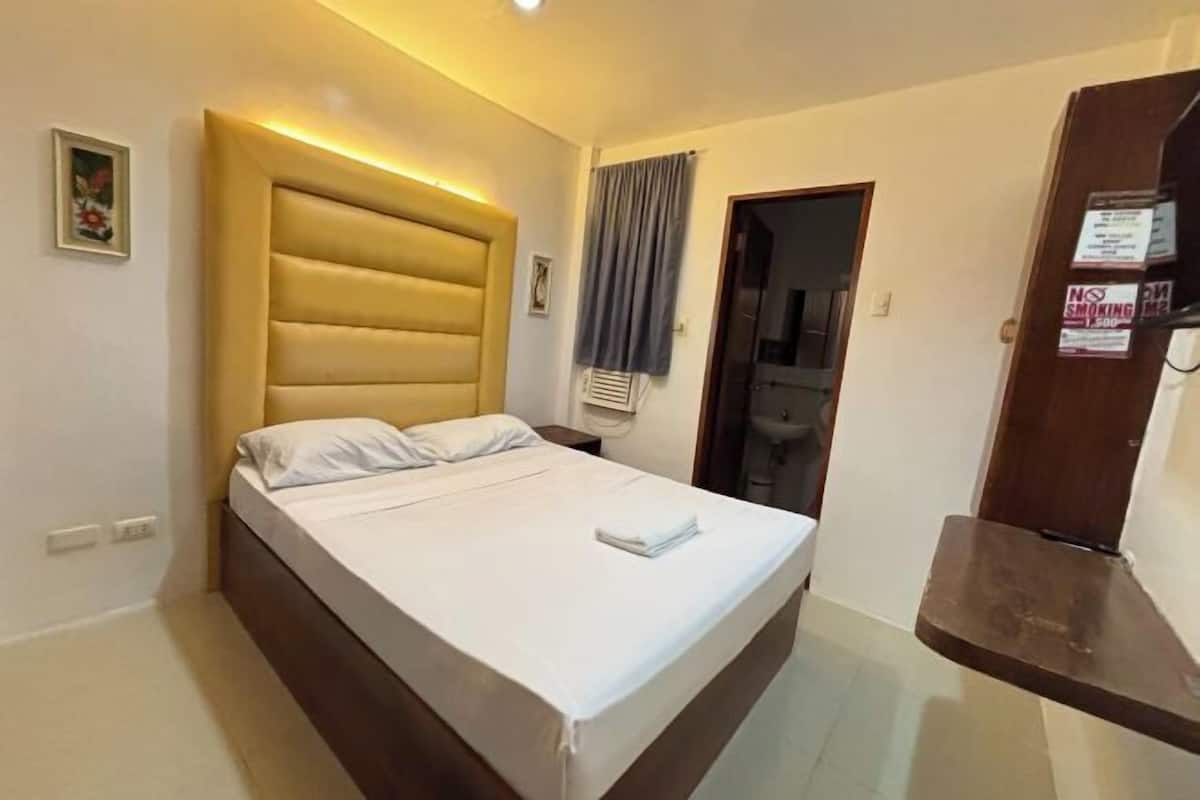 A hotel room with a bed, a nightstand, a mirror, and a door.