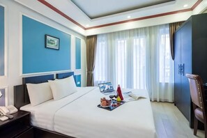 A hotel room with a bed, a desk with a phone, a laptop, and a tray with food.