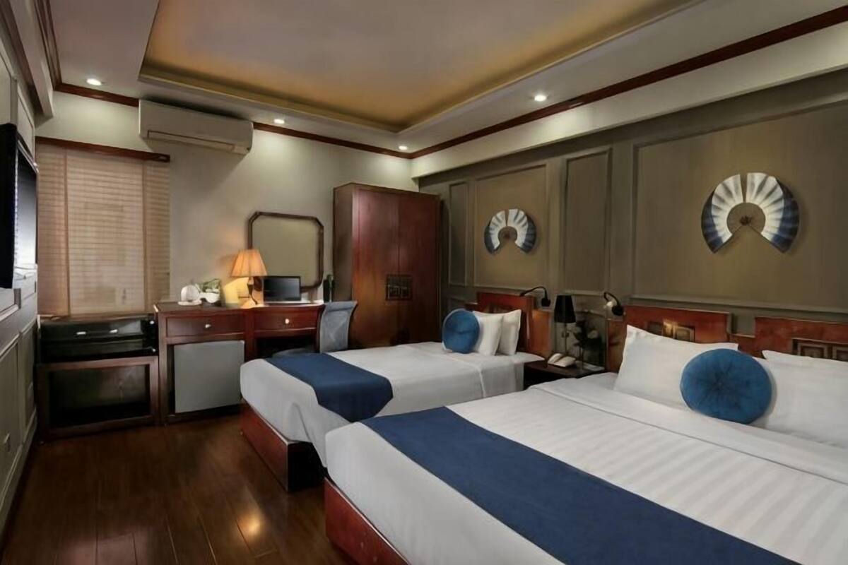 Une chambre d’hôtel avec deux lits, un bureau, une chaise, une télévision et une horloge murale.